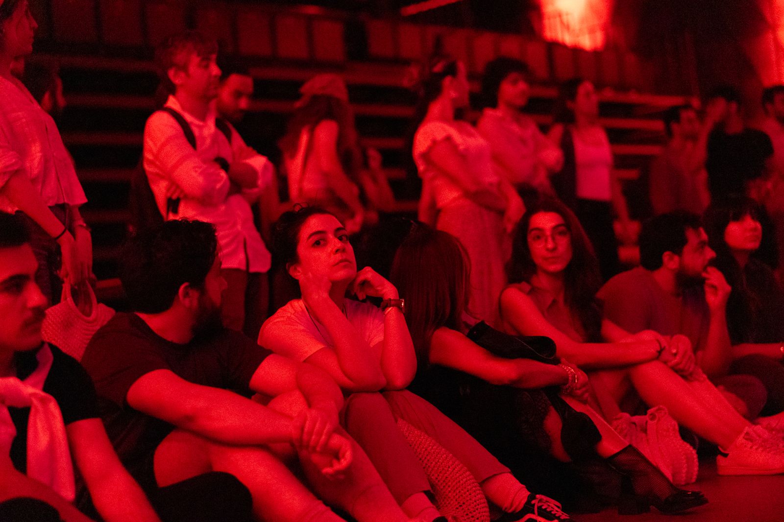 Kırmızı ışık altında yerde oturarak performansı izleyen seyirciler